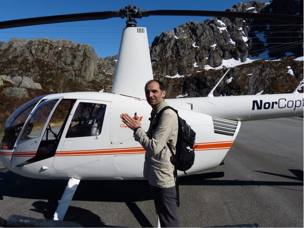 Alex Gladstone standing next to a helicopter with mountains in the backround